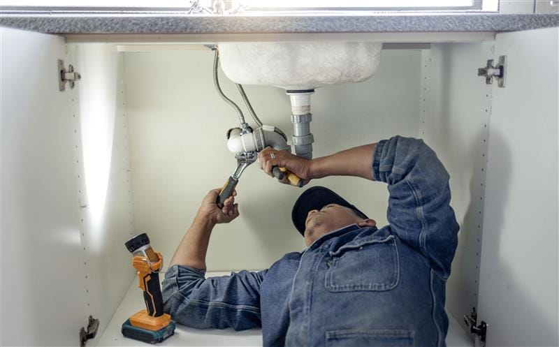 Plumber repairing pipes beneath a bathroom sink in Royal Palm Beach