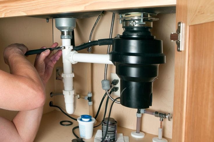 Plumber installing a garbage disposal beneath a kitchen sink in Royal Palm Beach