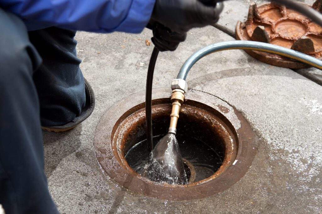 Plumber hydro jetting a sewer line through a manhole in Royal Palm Beach