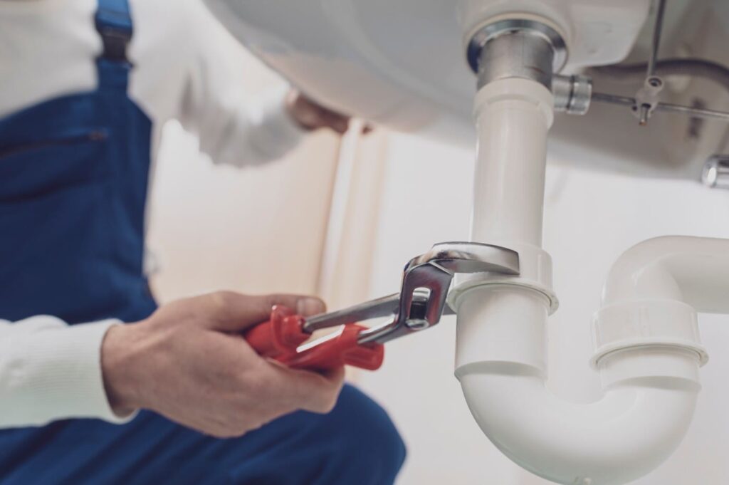 Plumber repairing a white drain pipe beneath a sink in Royal Palm Beach