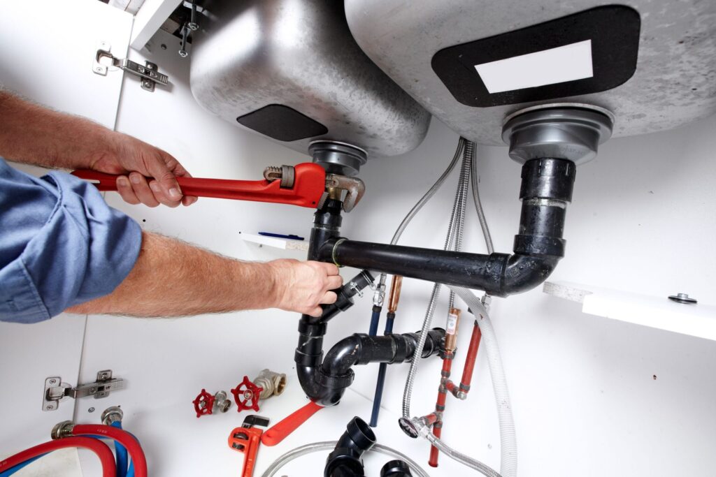 Plumber repairing drain pipes beneath a kitchen sink in Royal Palm Beach